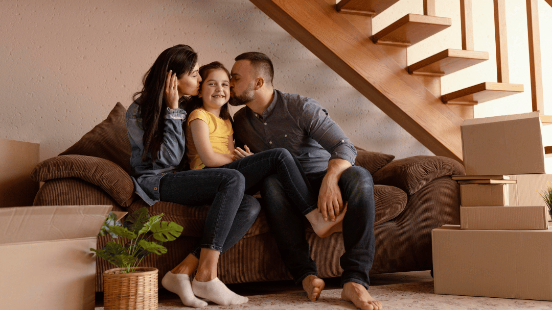 Família feliz, pai e mãe beijando a filha na sala sentados no sofá